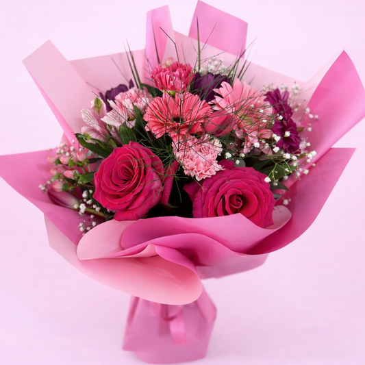 Bouquet of pink and red flowers wrapped in pink paper on a light pink background