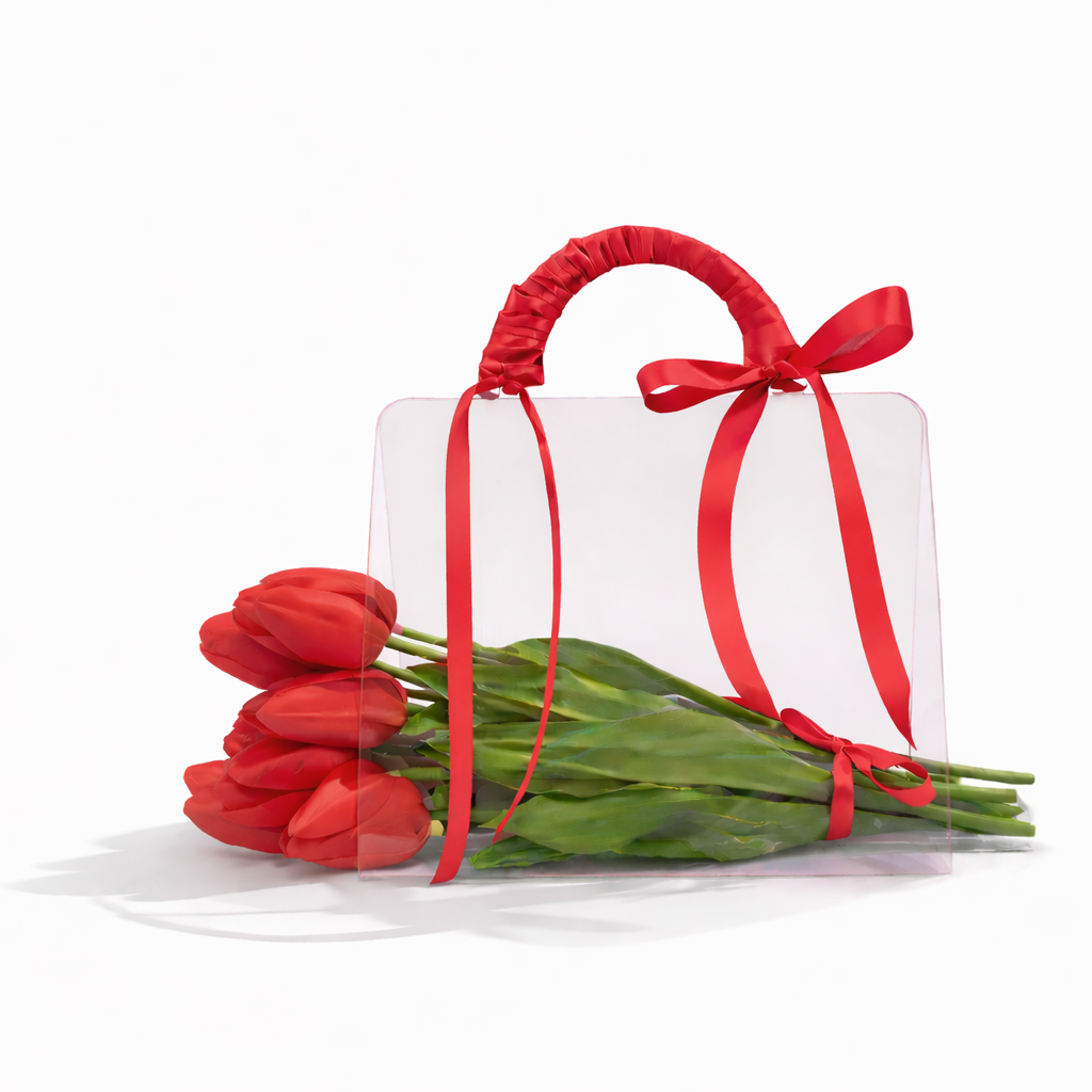 Red tulips tied with a red ribbon next to a white gift box on a white background