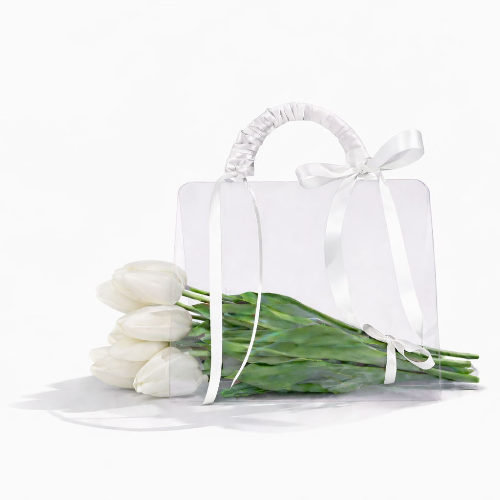 White tulips in a clear vase with a white ribbon on a white background
